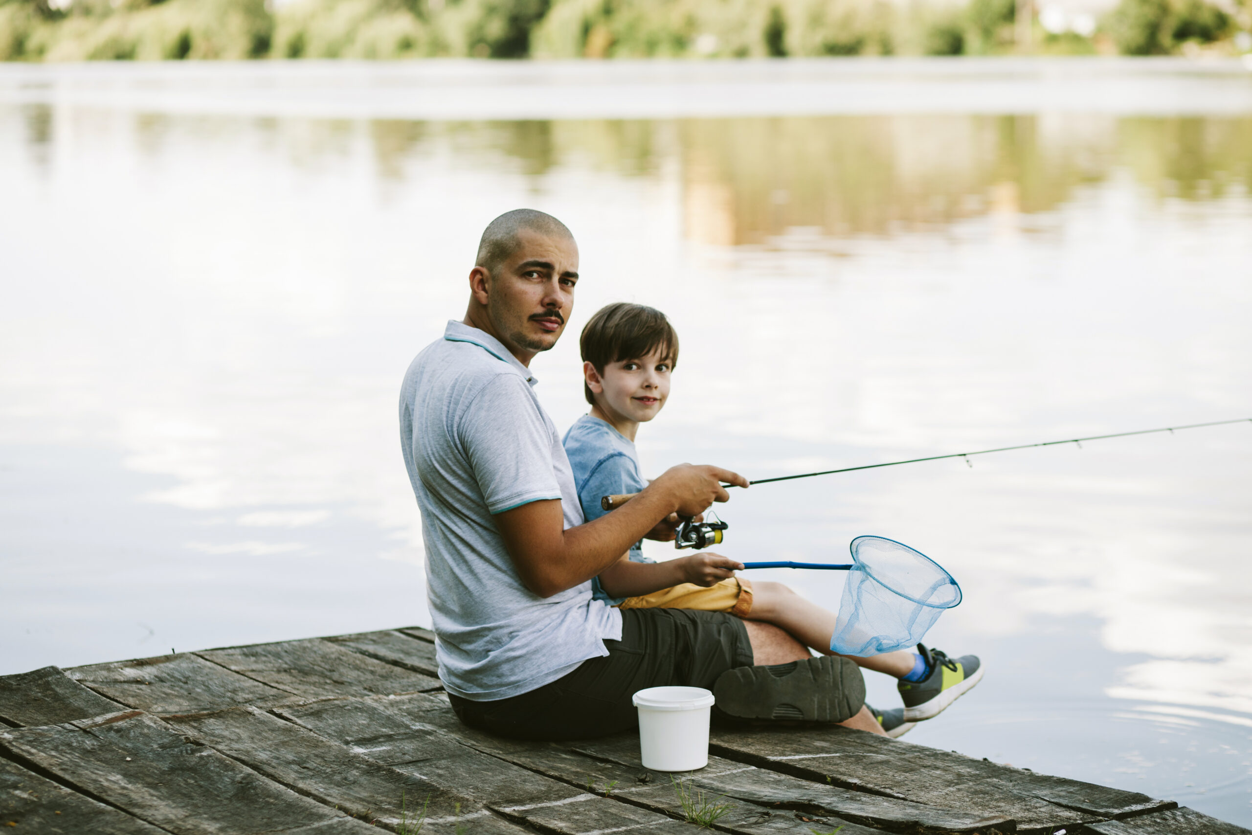 portrait-man-sitting-pier-with-his-son-fishing-lake